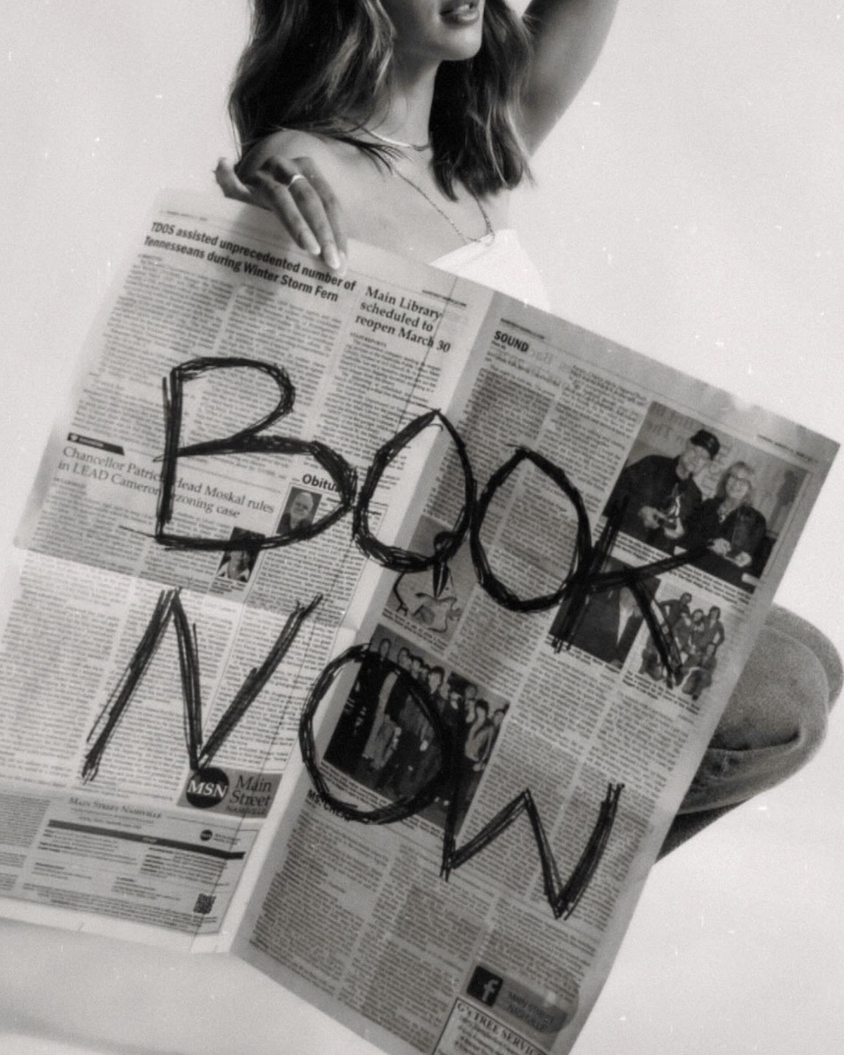 A Haven Lash Co. client holding up a newspaper hand-lettered with “Book Now”